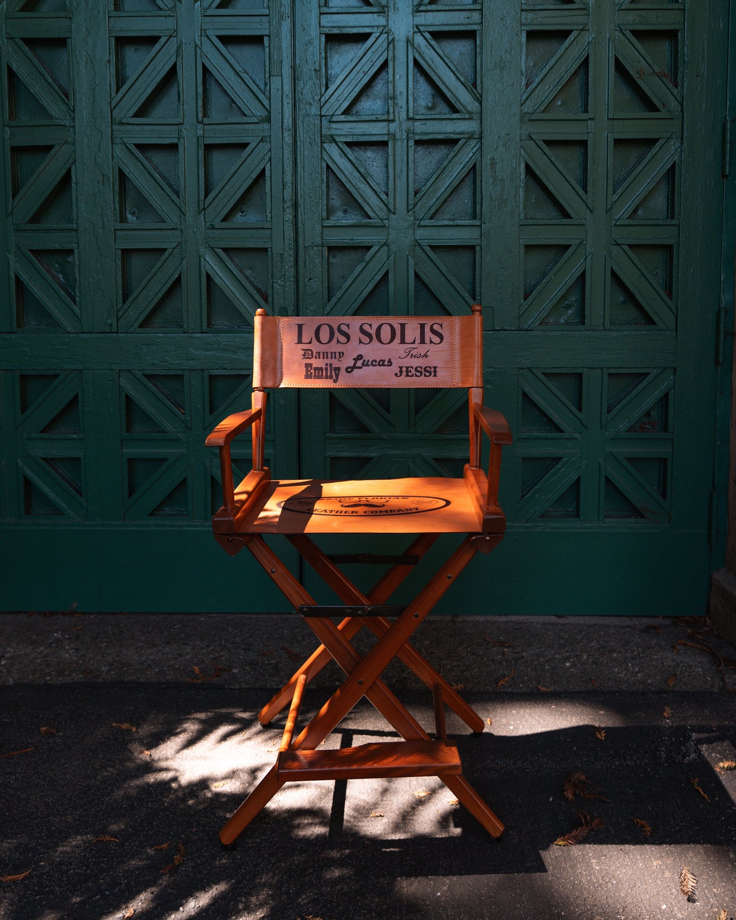 Wooden director's chair with 'Los Solis' and other st. florian branding against a green textured wall.